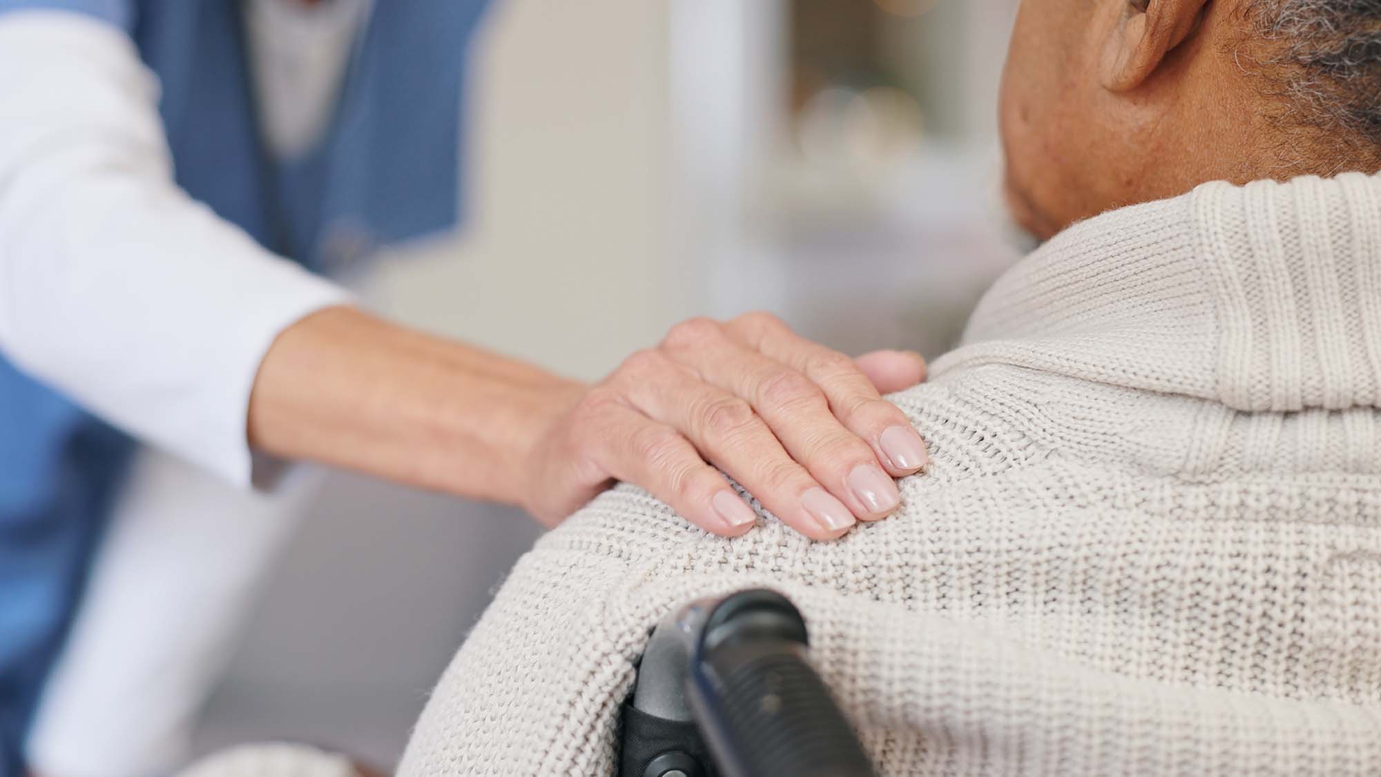 A carer touching the shoulde of an older man sitting in a wheelchair