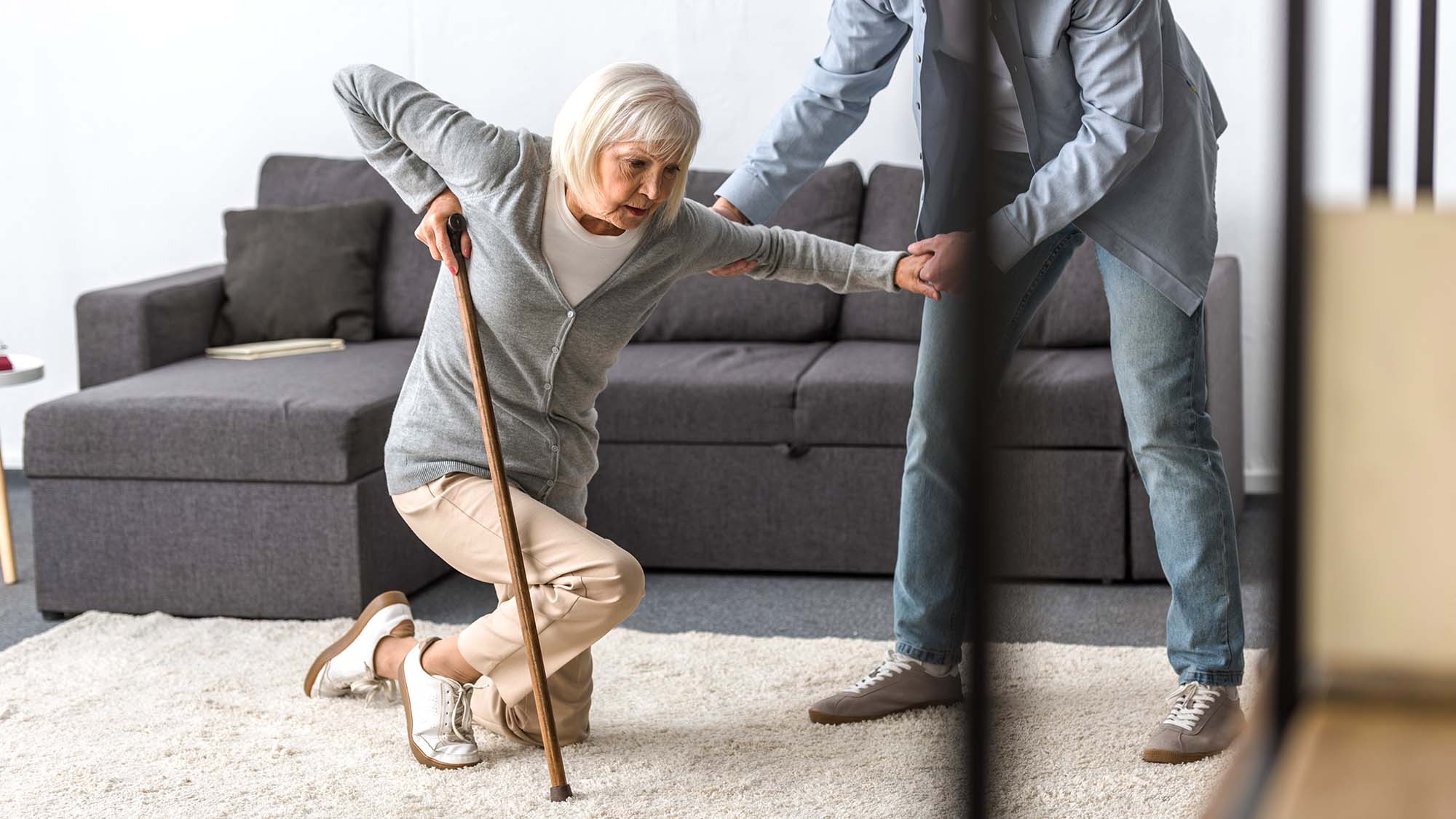 An older woman with a walking stick being helped to get up from the floor