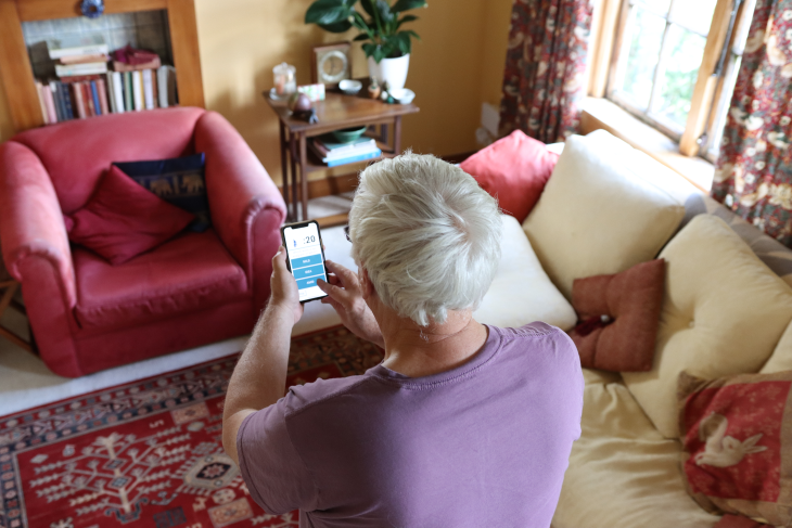 An older man smiling and sitting on a couch with his hands on a walking stick