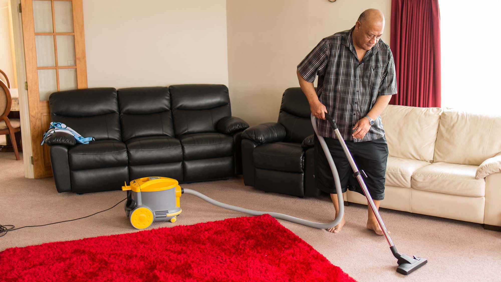 An older man vacuuming a bedroom carpet