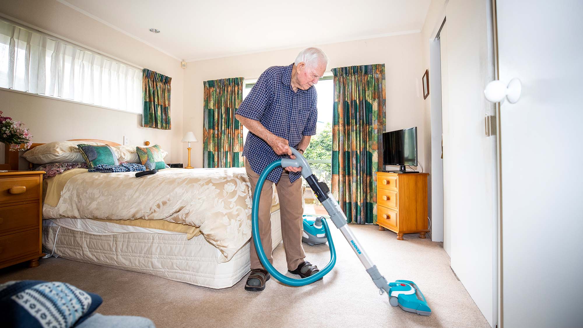 An older man vacuuming a bedroom carpet