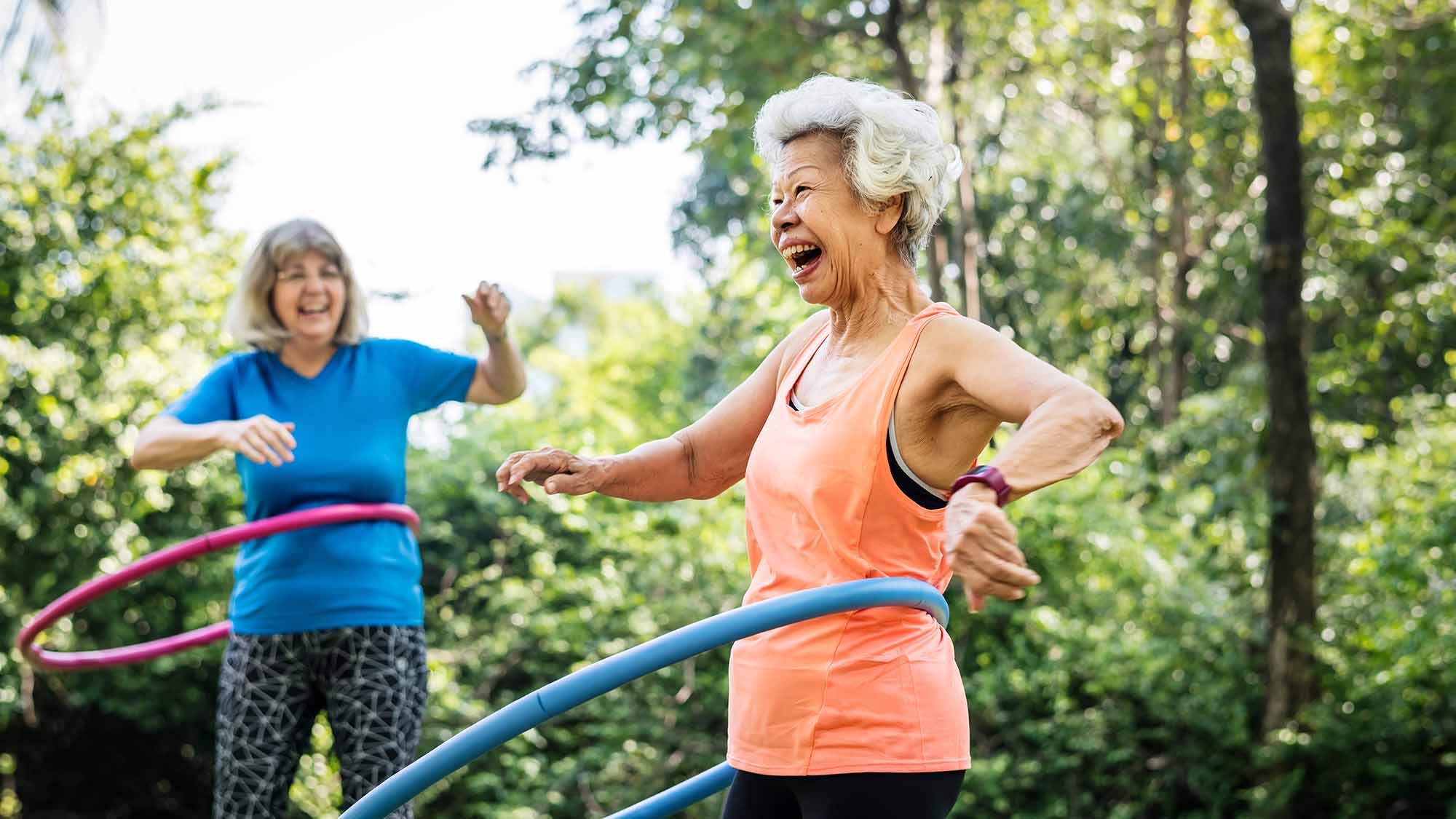 A laughing older woman doing exercises with hula hoops outside