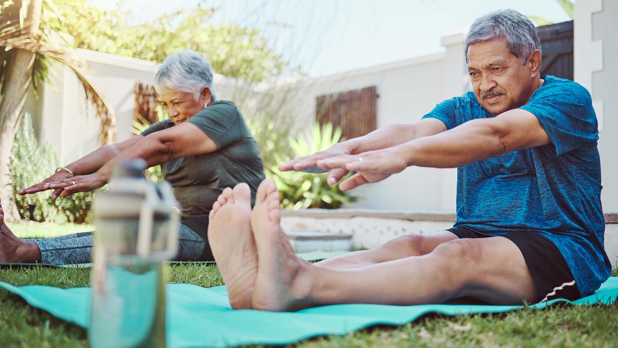 An older man and woman doing yoga outside