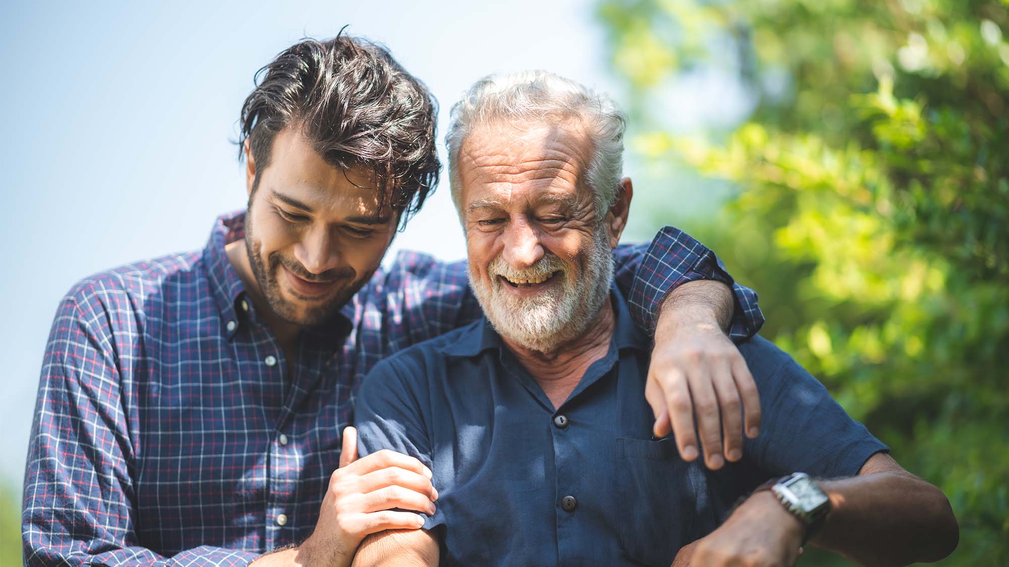 A laughing younger man with his arm around a laughing older man's shoulder